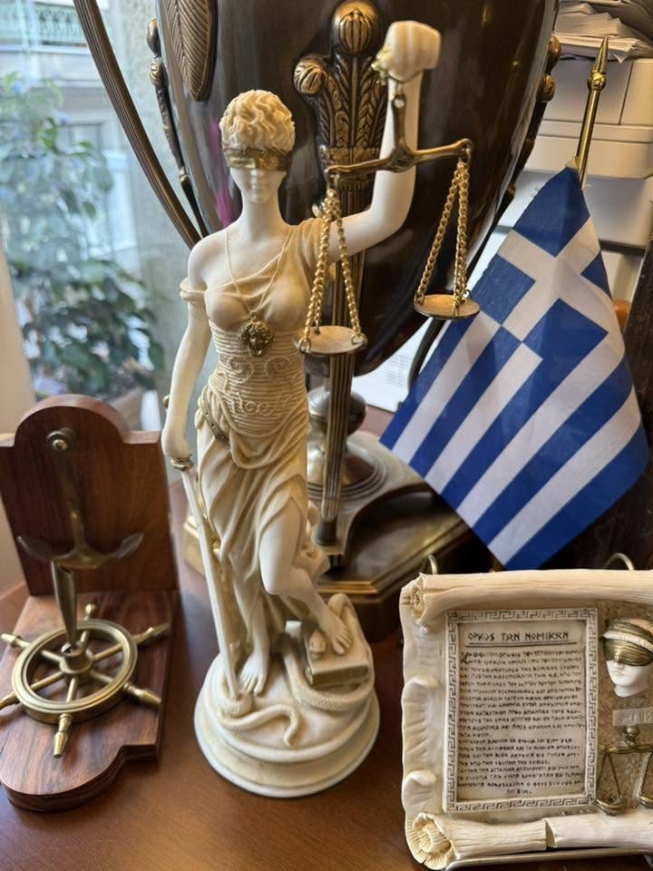 Λεπτομέρεια γραφείου: αγαλματίδιο της Δικαιοσύνης, ελληνική σημαία και πλακέτα με τον «Όρκο των Νομικών».